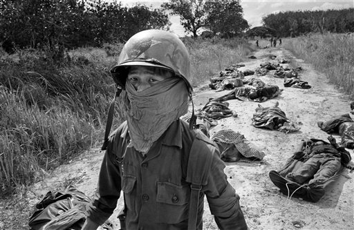  In this Nov. 27, 1965 file photo taken by Associated Press photographer Horst Faas, a Vietnamese litter bearer wears a face mask to keep out the smell as he passes the bodies of U.S. and Vietnamese soildiers killed in fighting against the Viet Cong 
