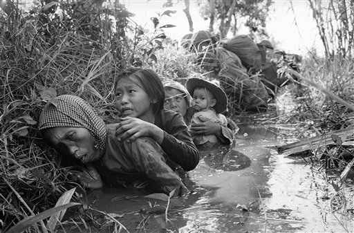 In this Jan. 1, 1966 file photo taken by Associated Press photographer Horst Faas, women and children crouch in a muddy canal as they take cover from intense Viet Cong fire at Bao Trai, about 20 miles west of Saigon, Vietnam. Faas, a prize-winning co
